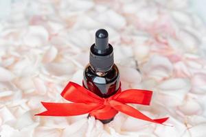 Homemade skincare natural rose essential oil product on Pink rose petals background in cosmetic dark glass bottle with dropper for moisturizing skin. Unbranded package mockup photo