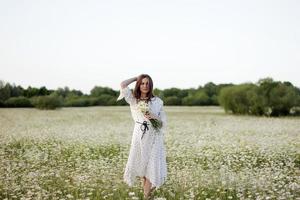 Beautiful young woman enjoying a field of daisies, beautiful girl relaxing outdoors, having fun, holding bouquet of daisies, happy young lady and spring-green nature, harmony concept. photo