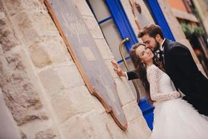 Wedding couple hugging in the old city. Blue vintage doors and cafe in ancient town on background. stylish bride in white long dress and groom in suit and bow tie. wedding day photo