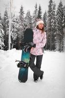 chica con una tabla de snowboard en las montañas. mujer joven sonriente feliz con snowboard en la montaña en invierno foto