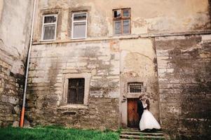 Happy newlywed couple hugging and kissing in old European town street, gorgeous bride in white wedding dress together with handsome groom. wedding day. photo