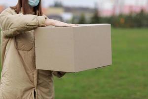 Delivery girl in face medical mask hold empty cardboard box outdoors on a residential complex background. Service coronavirus. Online shopping. mock up. photo