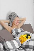 mujer feliz con flores de tulipán amarillo en la cama después de la ducha con una toalla en la cabeza disfrutando de un regalo romántico para el día de san valentín. le dio un ramo de flores. cumpleaños, día de la mujer, foto