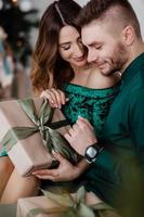 abriendo regalo de navidad. pareja enamorada feliz disfrutar de la celebración navideña. una pareja amorosa se abraza sonriendo mientras desempaca el fondo del árbol de navidad de regalo. Qué sorpresa. foto