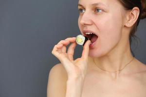 Closeup portrait of beautiful young funny woman eating and playing with sushi rolls on a grey background. Copy space photo