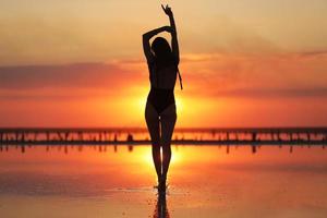 silhouette of a young slim woman in a swimsuit who dancing at sunset on the sea. summer holiday photo