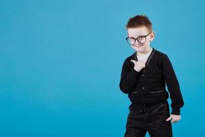 Like. Portrait of happy little schoolboy with glasses smiling at camera and doing thumbs up gesture, showing agree cool approval sign. indoor studio shot isolated on blue background photo