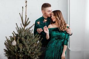 Burning sparklers in hands of party guests. Couple people are celebrating christmas and holidays happily near beautifully decorated christmas tree, christmas concept photo