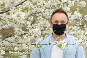 man in mask among flowering trees. man in a medical mask among a blossoming spring garden. Self-isolation and quarantine. cheerful man rejoices in the end of the pandemic and enjoys the spring. photo