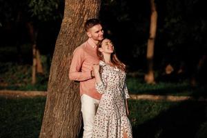 beautiful young couple in love hugging and smiling in the summer park. Stylish man in pink shirt and woman in dress are having fun together. love story. copy space photo