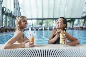 Poolside friends relaxing having healthy drinks. Sensual young women relaxing in spa swimming pool, spa indoor pool photo