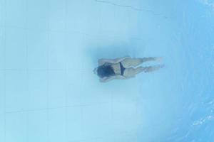 atractiva mujer joven flotando en una piscina con los brazos extendidos, mirando al cielo foto