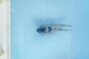 Drone view on young woman diving in blue swimming pool photo