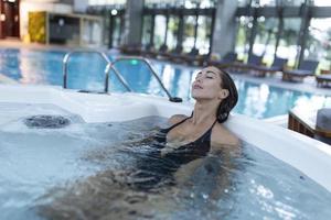 Excited female enjoys while splashing warm water during spa procedure in whirlpool