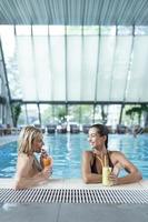 las amigas beben, cóctel mojito en el bar de la piscina, usan bikini hotel de lujo cerca de la playa en una isla tropical relajarse. hermosas mujeres jóvenes divirtiéndose en la piscina, bebiendo cócteles, sonriendo. foto