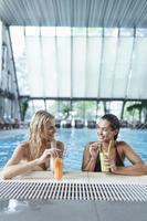 las amigas beben, cóctel mojito en el bar de la piscina, usan bikini hotel de lujo cerca de la playa en una isla tropical relajarse. hermosas mujeres jóvenes divirtiéndose en la piscina, bebiendo cócteles, sonriendo. foto