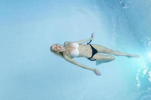 atractiva mujer joven flotando en una piscina con los brazos extendidos, mirando al cielo foto