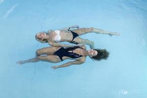 mujeres jóvenes relajándose y disfrutando junto a la piscina del spa de salud. están flotando en el agua de la piscina, usan bikini y se ven hermosos, serenos y despreocupados. foto
