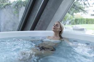 Excited female enjoys while splashing warm water during spa procedure in whirlpool photo