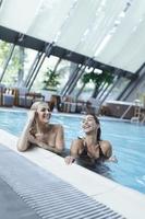 amigas hablando en la piscina, usan bikini hotel de lujo cerca de la playa en una isla tropical relajarse. hermosas mujeres jóvenes divirtiéndose en la piscina, sonriendo. foto