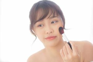 Beauty portrait young asian woman smile with face looking mirror applying makeup with brush cheek in the bedroom, beautiful of girl holding blusher, skin care and cosmetic concept. photo