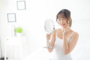 Beautiful face young asian woman with happy smiling and looking mirror, makeup of beauty facial girl with skincare and cosmetic treatment, refresh of female and clean for charming, healthy concept. photo