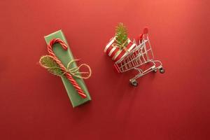 A shopping truck with a present box inside lying on a red background. Shopping and presents for Christmas holidays photo