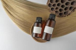 un aceite o suero para el cuidado del cabello en frascos cuentagotas marrones sobre una hebra de cabello rubio, maqueta de marketing de productos foto