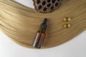 A brown dropper bottle and golden capsules for face care lying on a strand of blonde hair photo