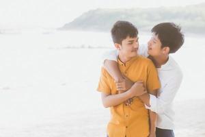 retrato homosexual joven pareja asiática de pie abrazo juntos en la playa en verano, turismo gay de asia para el ocio y relajarse con romanticismo y felicidad en vacaciones en el mar, concepto lgbt. foto