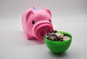 hucha de cerdo rosa con montón de monedas en taza verde sobre fondo blanco concepto cuenta de ahorros banco de ahorro negocio financiero foto