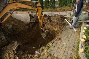 un albañil trabaja en un sitio de construcción mientras una excavadora draga un agujero para un pozo negro foto