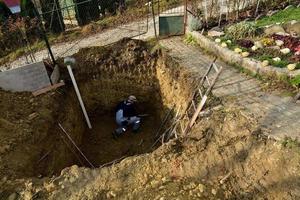 un albañil trabaja en un sitio de construcción mientras una excavadora draga un agujero para un pozo negro foto