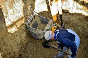 trabajador carga manualmente piedras en la pala de una excavadora durante la excavación de un pozo negro foto