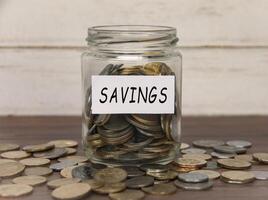 Savings label on coin jar on top of wooden desk with asorted coins background. photo