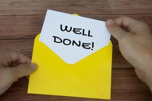 Well done text on white notepad with hand opening the envelope. Motivational concept photo