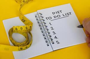 Diet plan text on white notepad with measuring tape on yellow background. Health and diet concept photo