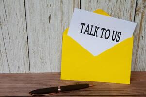 Talk to us text on white notepad in yellow envelope. Customer service concept photo