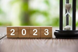 Year 2023 text on wooden blocks with minute glass and blurred nature background. New year concept 2023 photo