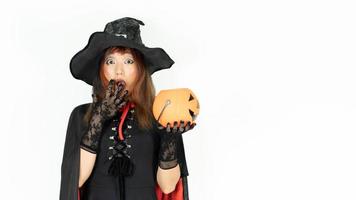 A girl with black and orange hair  in black dress and witch hat is holding pumpkin with wow emotion. Halloween day photo