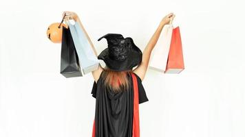 Beautiful girl with black and orange hair  in black dress and turn around witch hat is holding shopping bags. Halloween concept photo