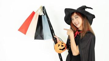 Asian girl with black and orange hair  in black dress and witch hat is holding staff and pumpkin isolated on white background. Emotion smile photo