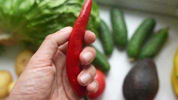 Chef hand holds a red pepper with other fresh produce in background video