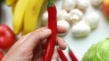 Hand holds red cayenne pepper  with other fresh produce in background video