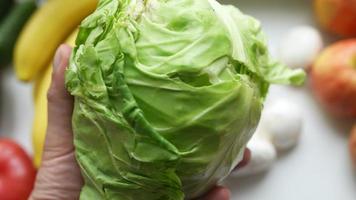 Hand holds a head of cabbage with other produce in background video