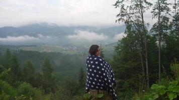 Young woman wrapped in a polka dot blanket looks out over a foggy forest video