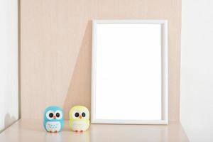 two little owl statues next to white empty frame on a bedside table in kids room. copy space for inscription photo