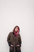 young woman with pink hair piercings and tattoos against wall with copy space photo