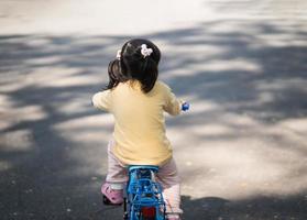 niña asiática aprendiendo a andar en bicicleta en el jardín del parque. concepto de educación para niños que practican ciclismo en el parque, concepto de deporte para bebés. foto