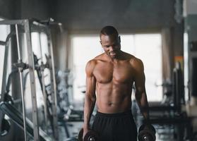 African sport man strong muscle working out excercise in weights with dumbbell at fitness room at the gym. Body building sport man fitness concept. photo